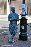 Statue of George Formby leaning on a lamppost on the corner of the street in Douglas, Isle of Man